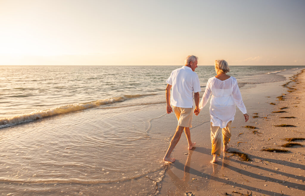 Senior couple walking hand in hand along a beach at sunset