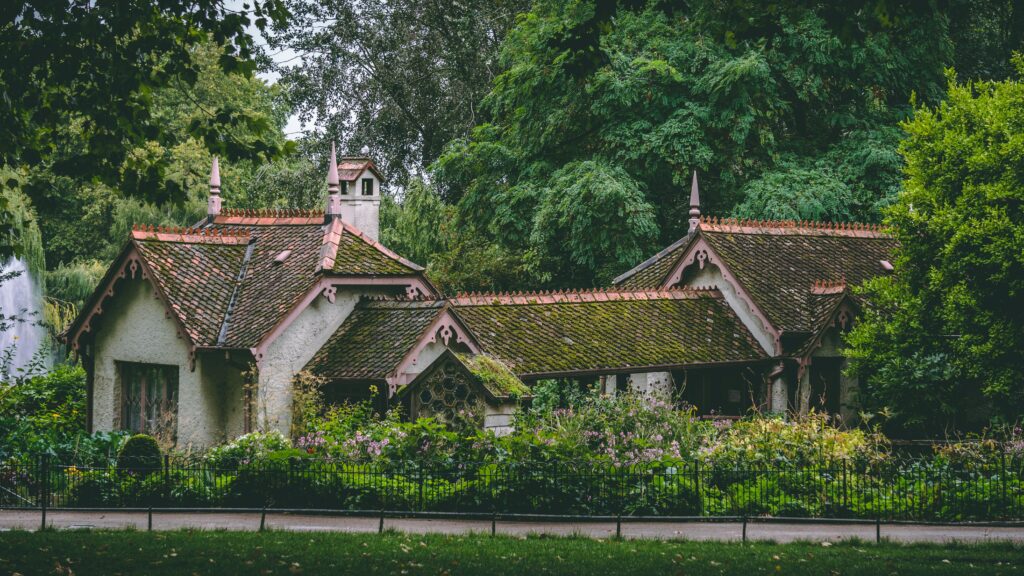 Charming cottage with a tiled roof and decorative gables surrounded by lush trees and garden planting.
